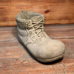 May include: A grey concrete boot planter with a lace-up design. The boot is a decorative planter for small plants or flowers.