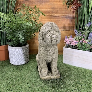 May include: A grey stone sculpture of a sitting poodle dog. The sculpture is detailed with textured fur and a realistic expression. The dog is sitting on a textured base.