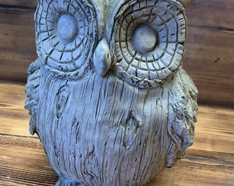May include: A grey stone owl figurine with large, detailed eyes. The owl is perched on a wooden surface.