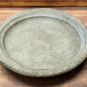 May include: A round, grey concrete bird bath with a decorative, scalloped edge.