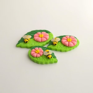 May include: Three green leaf-shaped decorations with pink flowers and yellow and black bees.