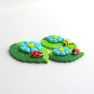 Peut inclure: Trois fleurs bleues avec des centres jaunes sur des feuilles vertes avec une coccinelle et une abeille sur le dessus.