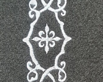 May include: White embroidered design on a black fabric background. The design features a repeating pattern of stylised flowers and swirls. The text "Borduren Tantangara" is visible at the bottom of the image.