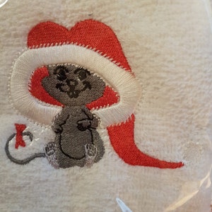 May include: A white towel with a gray mouse wearing a red Santa hat embroidered on it.