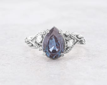 May include: A pear-shaped, purple gemstone ring set in a silver band with a delicate, vine-like design accented with smaller white gemstones.