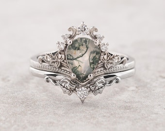 May include: A silver ring set with a pear-shaped green moss agate gemstone surrounded by a delicate floral design and smaller clear gemstones.