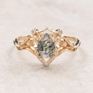Può includere: Un anello d'oro con una pietra preziosa di agata muschiata a forma di pera, circondata da una delicata montatura ornata di piccoli diamanti.