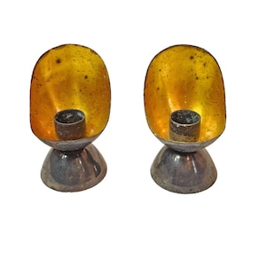 May include: A pair of gold and silver candle holders. The candle holders are shaped like a bowl with a round base. The candle holders are made of metal and have a shiny finish.