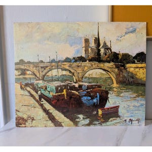 May include: Oil painting depicting a Parisian scene with a bridge, boats, and the Notre Dame Cathedral. The artwork features a bridge with multiple arches, boats docked on the river, and the cathedral in the background. The color palette includes blues, browns, and greens.