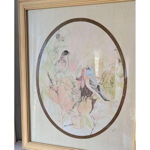 May include: Framed artwork featuring two birds perched on branches with pink and green foliage. The birds have black, blue, and tan feathers. The artwork is set within a brown oval and a gold-colored frame.