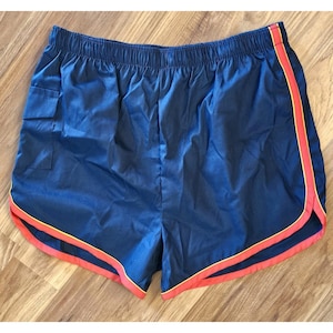 Puede incluir: Pantalones cortos deportivos azul marino con ribete rojo y amarillo. Los pantalones cortos tienen un pequeño bolsillo en el lado izquierdo y una cintura elástica. Estos pantalones cortos para correr están hechos de un material ligero, posiblemente nailon.