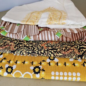 May include: Four different fabric swatches stacked on top of each other. The top swatch is white with a gold embroidered design. The second swatch is brown and white striped with green diamond shapes. The third swatch is black and yellow with a floral pattern. The bottom swatch is yellow with a white and black floral pattern.