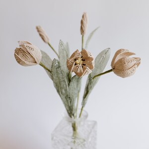 May include: A bouquet of beige beaded tulips with green beaded leaves in a clear glass vase.