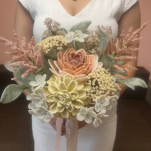 May include: A beaded bouquet of flowers in shades of peach, cream, and green. The bouquet features a large peach-colored flower in the center, surrounded by smaller cream-colored flowers and green foliage.