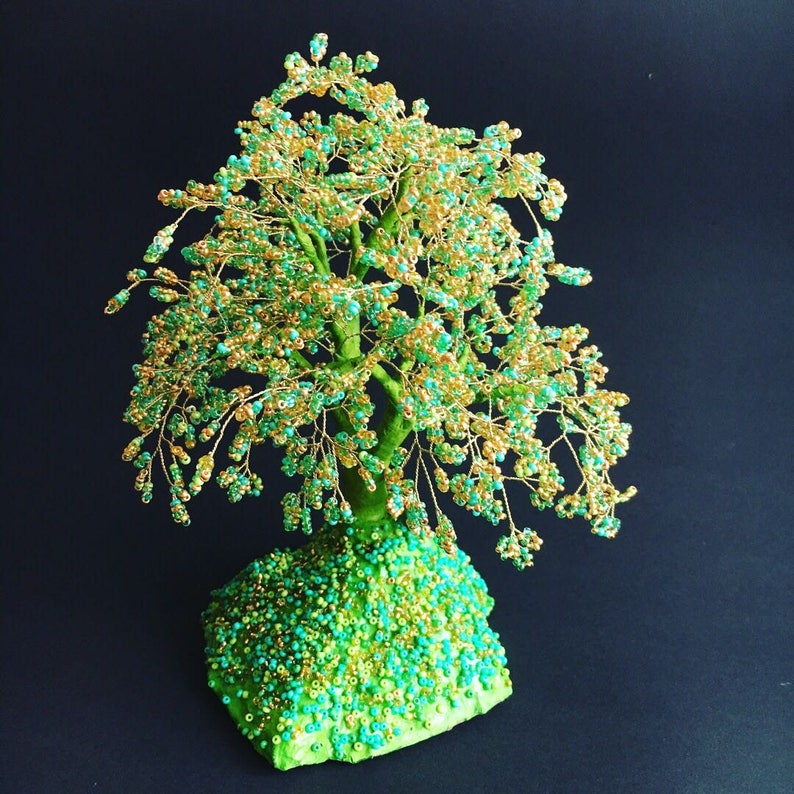 K&ouml;nnte beinhalten: Eine Perlenbaumskulptur mit einer gr&uuml;n-goldenen Basis. Der Baum besteht aus Draht und Perlen, und die &Auml;ste sind mit kleinen, gr&uuml;n-goldenen Perlen bedeckt.