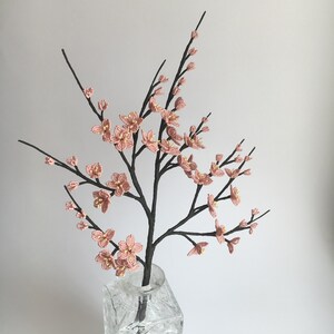 May include: A delicate pink beaded flower arrangement in a clear glass vase. The flowers are arranged in a cascading style, creating a beautiful and elegant display.