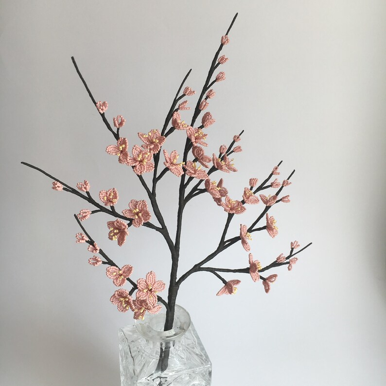 May include: A delicate pink beaded flower arrangement in a clear glass vase. The flowers are arranged in a cascading style, creating a beautiful and elegant display.