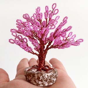 May include: A pink beaded wire tree sculpture with a brown wire base and a textured brown and white base.