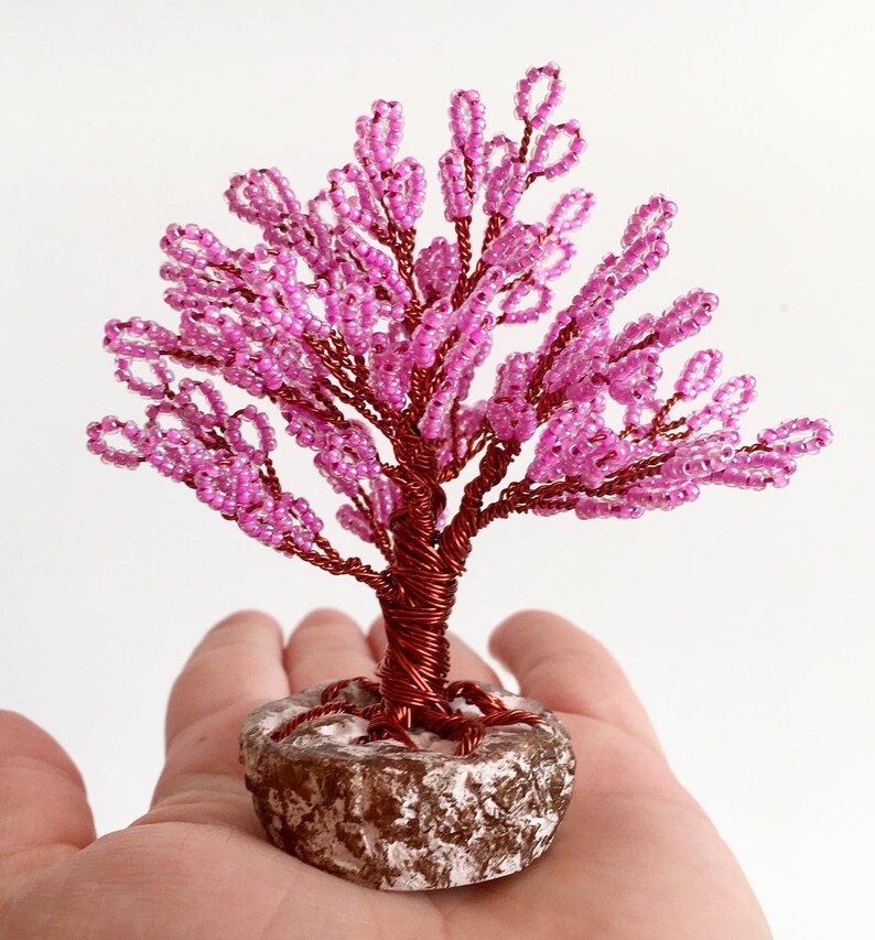 May include: A pink beaded wire tree sculpture with a brown wire base and a textured brown and white base.