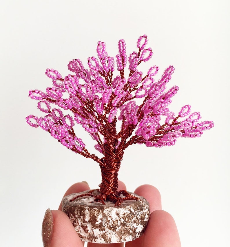 May include: A pink beaded wire tree sculpture with a brown wire trunk and a white base.