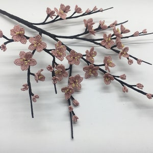 May include: A delicate branch with pink and yellow beaded blossoms, resembling a cherry blossom tree. The branch is made of black wire and the flowers are crafted with small beads.