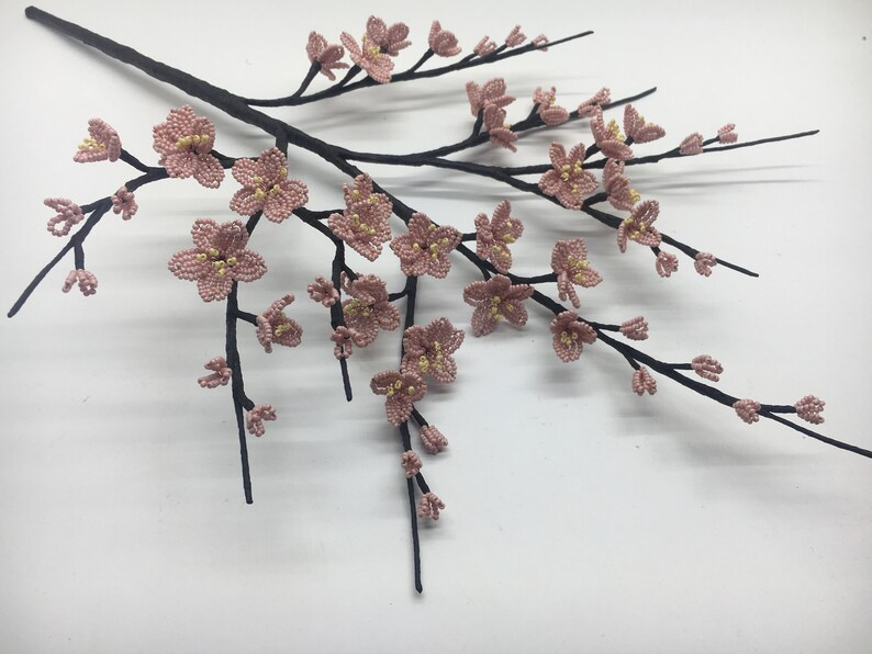 May include: A delicate branch with pink and yellow beaded blossoms, resembling a cherry blossom tree. The branch is made of black wire and the flowers are crafted with small beads.