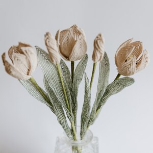 May include: A bouquet of beige beaded tulips with green beaded stems in a clear glass vase.