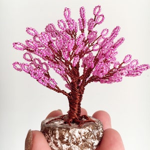 May include: A pink beaded wire tree sculpture with a brown wire trunk and a brown base.