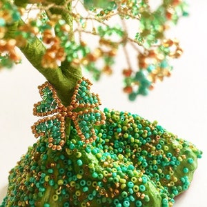 K&ouml;nnte beinhalten: Ein Perlen-Drahtbaum mit gr&uuml;nen und goldenen Bl&auml;ttern. Der Baum ist mit einer gr&uuml;nen und goldenen Perlen Schleife verziert.