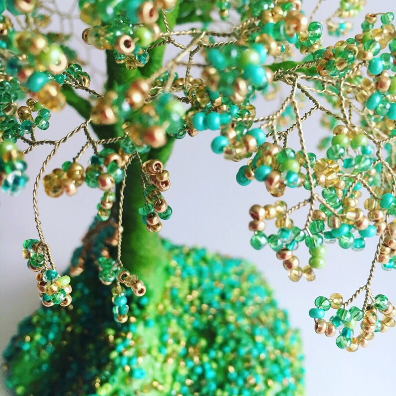 K&ouml;nnte beinhalten: Eine Drahtskulptur eines Baumes, die mit gr&uuml;nen und goldenen Perlen verziert ist. Der Baum besteht aus d&uuml;nnen Drahtzweigen und hat eine gr&uuml;ne Basis.