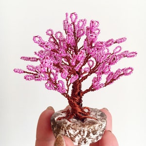 May include: A pink beaded wire tree sculpture with a brown wire trunk and a stone base.