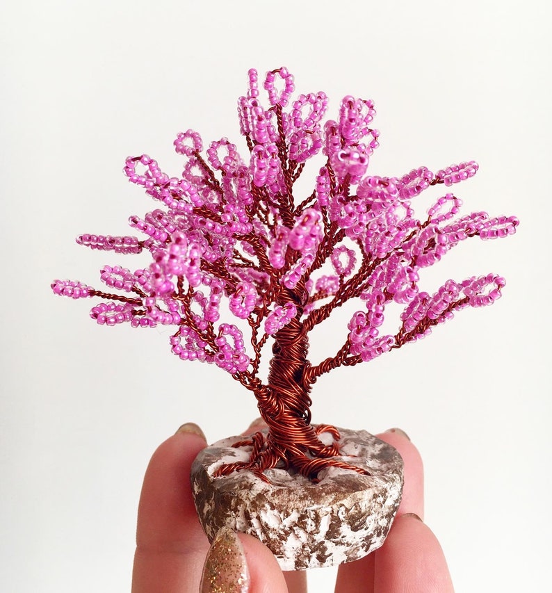 May include: A pink beaded wire tree sculpture with a brown wire trunk and a stone base.