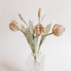 May include: A bouquet of beige beaded tulips in a clear glass vase. The tulips have green beaded stems and leaves.