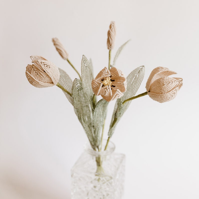 May include: A bouquet of beige beaded tulips in a clear glass vase. The tulips have green beaded stems and leaves.