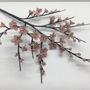 May include: A delicate branch with pink beaded blossoms, resembling a cherry blossom tree. The branch is made of black wire and the flowers are crafted with small pink and yellow beads.