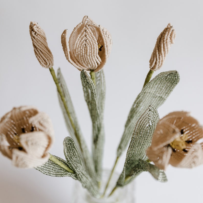 May include: A bouquet of beaded tulips with beige and brown petals and green leaves. The tulips are arranged in a vase.