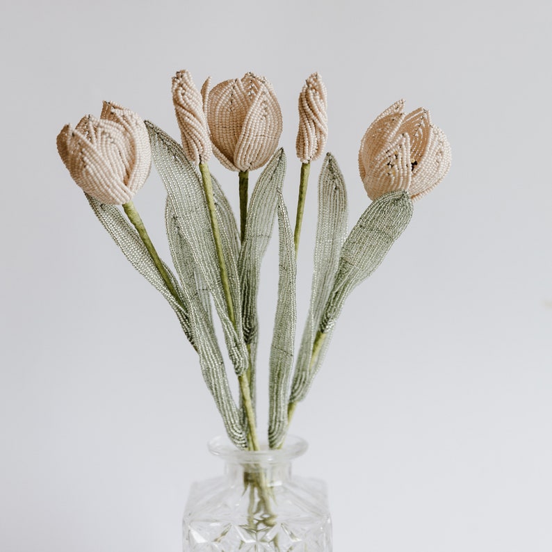 May include: A bouquet of five cream-colored beaded tulips with green beaded stems in a clear glass vase.