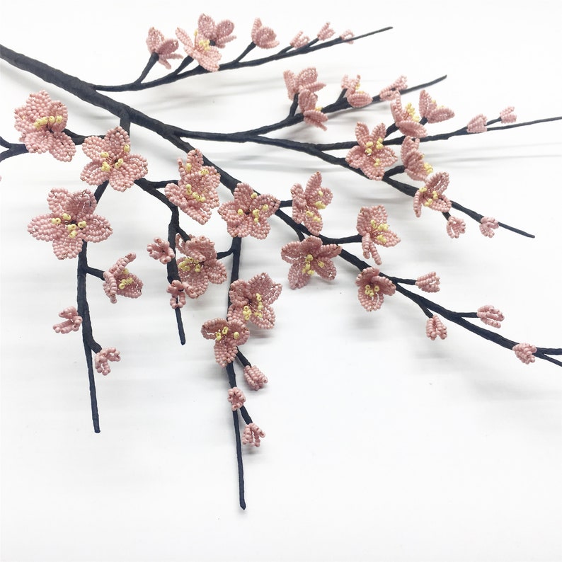 May include: A delicate branch with pink beaded blossoms, resembling cherry blossoms, on a white background.
