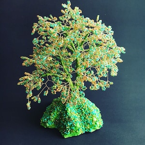 K&ouml;nnte beinhalten: Eine Drahtskulptur eines Baumes mit gr&uuml;nen und goldenen Perlen, die auf einem gr&uuml;nen Sockel steht. Der Baum besteht aus Draht und Perlen, der Sockel aus einem gr&uuml;nen Material.