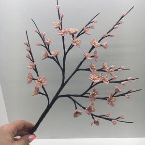 May include: A delicate branch with pink and yellow beaded flowers, crafted with intricate detail. The branch is made of black wire and is perfect for adding a touch of spring to any decor.