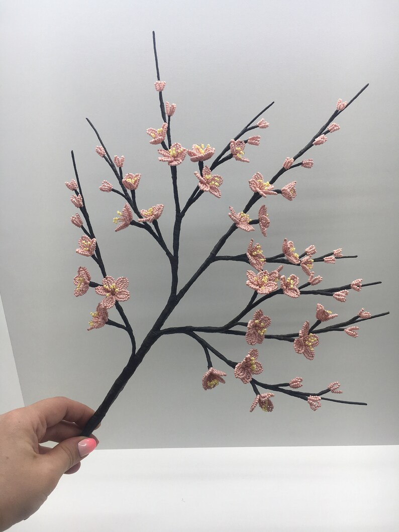 May include: A delicate branch with pink and yellow beaded flowers, crafted with intricate detail. The branch is made of black wire and is perfect for adding a touch of spring to any decor.