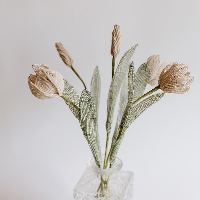 May include: A bouquet of delicate, blush-colored beaded tulips with green beaded leaves in a clear glass vase.