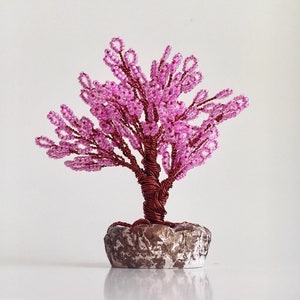 May include: A pink beaded wire tree sculpture with a brown wire trunk and a gray stone base.
