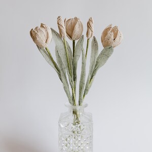 May include: A bouquet of five cream-colored beaded tulips with green beaded stems in a clear glass vase with a diamond pattern.