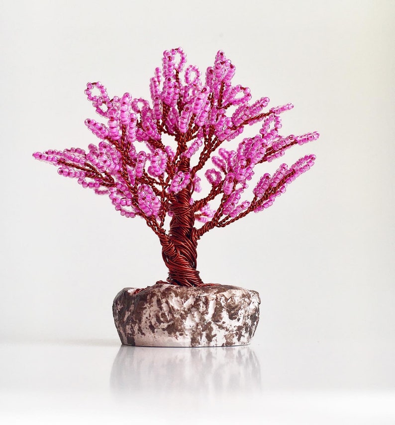 May include: A pink beaded wire tree sculpture with a brown wire trunk and a gray stone base.