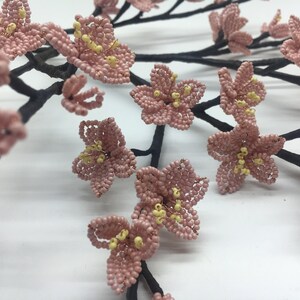 May include: A delicate branch of pink beaded flowers with yellow centres. The flowers are arranged in a cluster and are attached to a black wire branch.