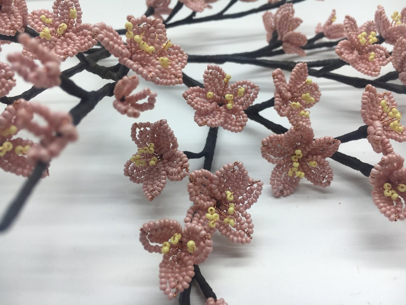 May include: A delicate branch of pink beaded flowers with yellow centres. The flowers are arranged in a cluster and are attached to a black wire branch.