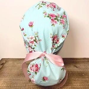 Surgical scrub cap with ponytail. light blue with pink spring flowers and pink ribbon.
