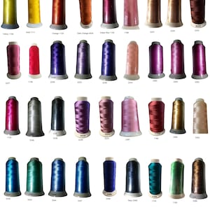 Op de afbeelding: Een verzameling kleurrijke borduurgaren spoelen, elk gelabeld met een nummer. De draden vari&euml;ren in kleur, waaronder geel, oranje, rood, roze, paars, blauw, groen en bruin. De spoelen zijn in nette rijen gerangschikt.