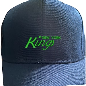 May include: A navy blue baseball cap with the words "Kings New York" embroidered in green. The cap has a curved brim and a structured crown, suitable for casual wear.